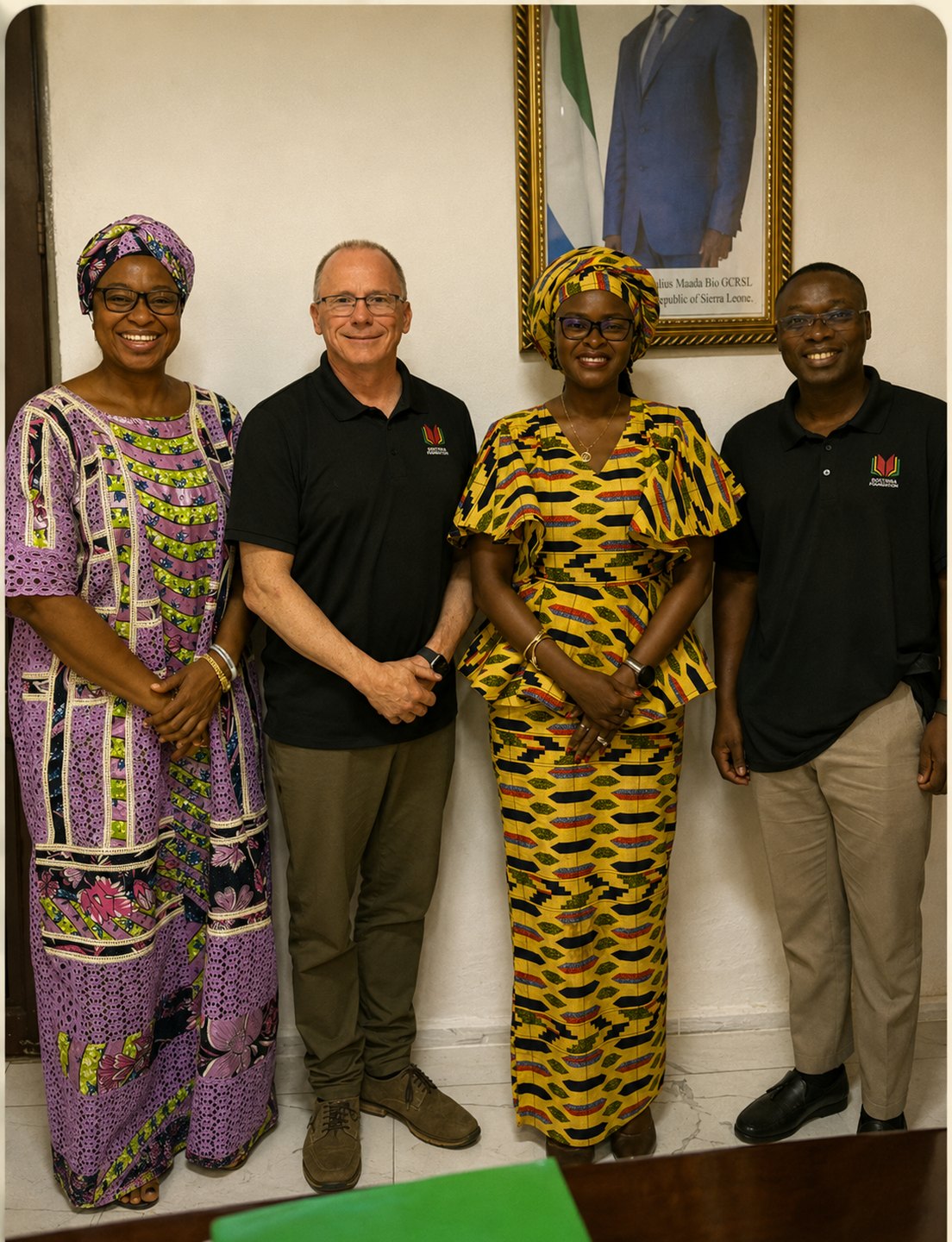 Doctrina Foundation staff standing with Sierra Leone government partners beneath a portrait of the President